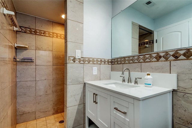 full bath featuring visible vents, a tile shower, tile walls, and vanity