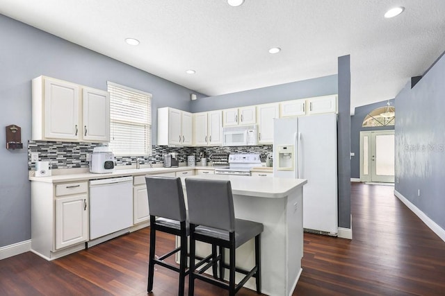 kitchen featuring tasteful backsplash, white appliances, a breakfast bar, a kitchen island, and white cabinetry