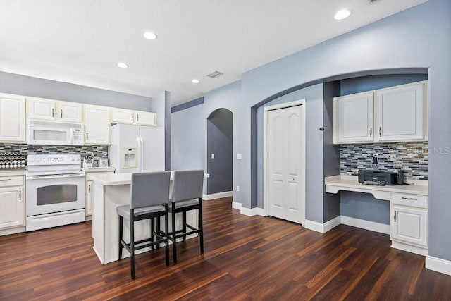 kitchen with white appliances, a breakfast bar area, dark wood-type flooring, and white cabinets