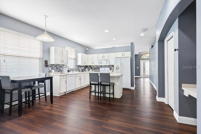 kitchen featuring hanging light fixtures, a breakfast bar area, white appliances, a center island, and backsplash