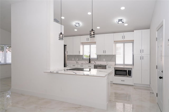 kitchen with appliances with stainless steel finishes, white cabinetry, hanging light fixtures, tasteful backsplash, and kitchen peninsula