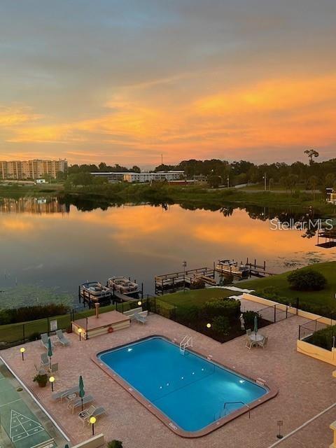 pool at dusk with a patio area and a water view