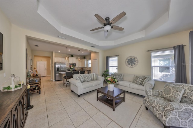 tiled living room with ceiling fan and a tray ceiling