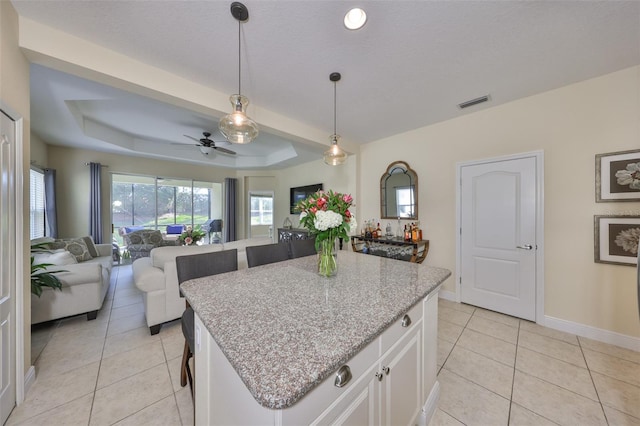 kitchen with a kitchen island, pendant lighting, white cabinets, light tile patterned floors, and a raised ceiling