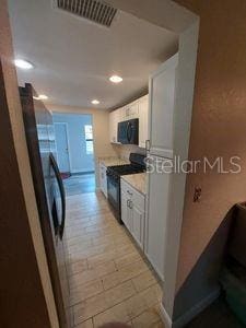 kitchen with black appliances, visible vents, and white cabinets