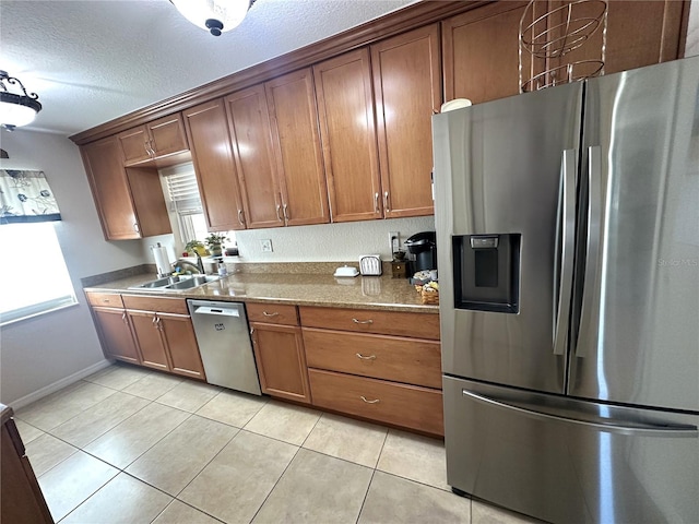 kitchen with stainless steel appliances, sink, light tile patterned floors, a textured ceiling, and dark stone countertops