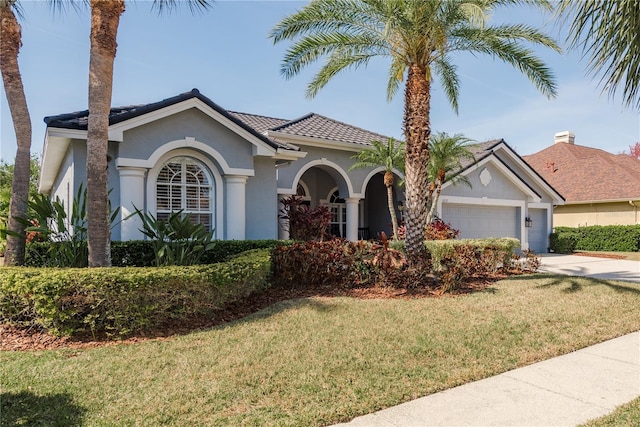 view of front facade with a garage, concrete driveway, a tile roof, a front lawn, and stucco siding