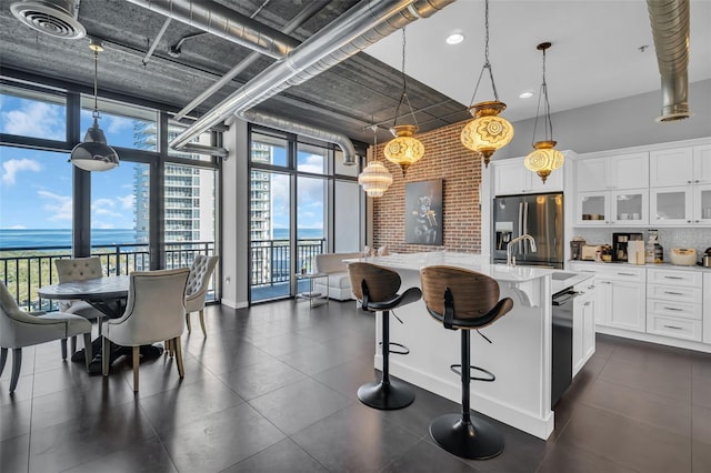 kitchen with a water view, pendant lighting, stainless steel fridge with ice dispenser, white cabinetry, and a kitchen island with sink