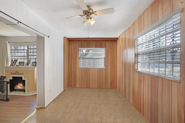 unfurnished room featuring a wealth of natural light, ceiling fan, and wood walls