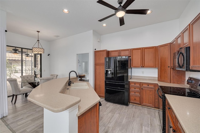 kitchen with light hardwood / wood-style flooring, an island with sink, black appliances, decorative light fixtures, and sink