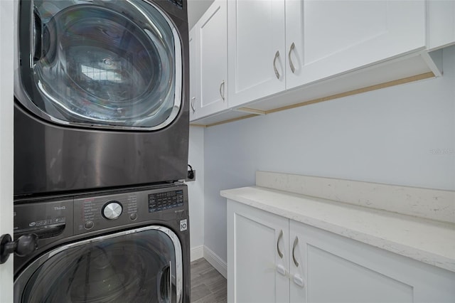 clothes washing area with stacked washing maching and dryer, cabinets, and wood-type flooring