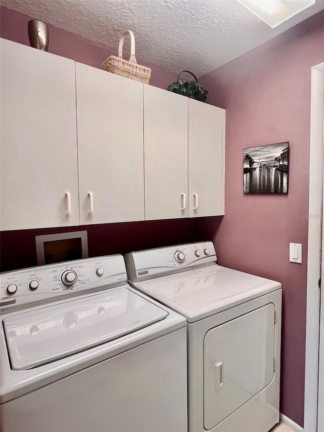 washroom with cabinets, washing machine and clothes dryer, and a textured ceiling