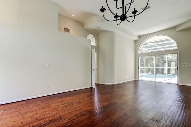 spare room featuring an inviting chandelier, a towering ceiling, and hardwood / wood-style floors