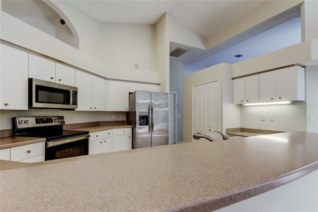 kitchen featuring appliances with stainless steel finishes, white cabinetry, sink, a high ceiling, and kitchen peninsula