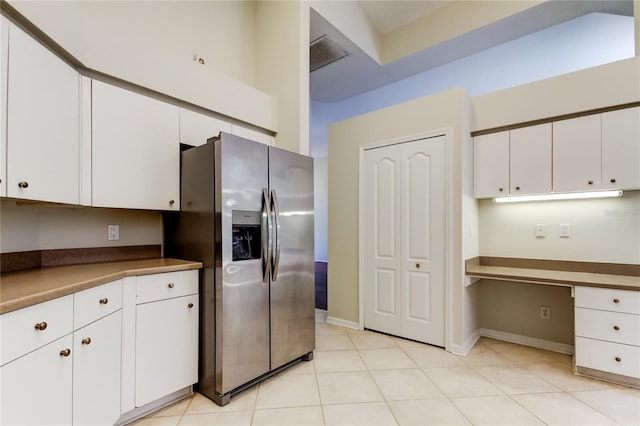 kitchen with white cabinets, built in desk, stainless steel fridge, and light tile patterned floors