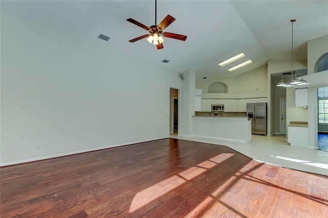 unfurnished living room with high vaulted ceiling, ceiling fan with notable chandelier, and light wood-type flooring