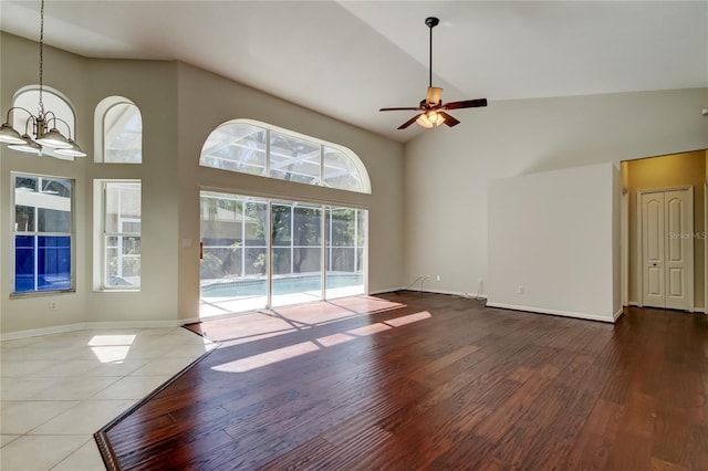 unfurnished living room featuring hardwood / wood-style floors, ceiling fan with notable chandelier, and high vaulted ceiling