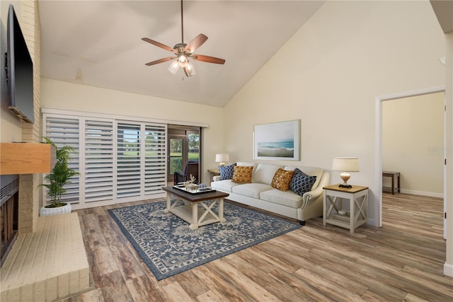 living room featuring baseboards, ceiling fan, wood finished floors, a fireplace, and high vaulted ceiling