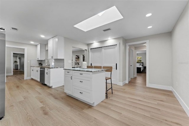 kitchen with white cabinetry, a skylight, tasteful backsplash, and dishwasher