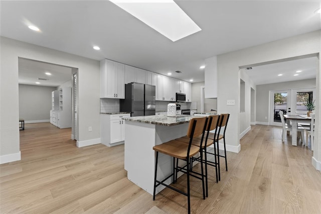 kitchen with stainless steel appliances, backsplash, light stone counters, white cabinets, and a kitchen breakfast bar