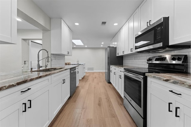 kitchen with stainless steel appliances, light stone counters, white cabinets, sink, and light wood-type flooring