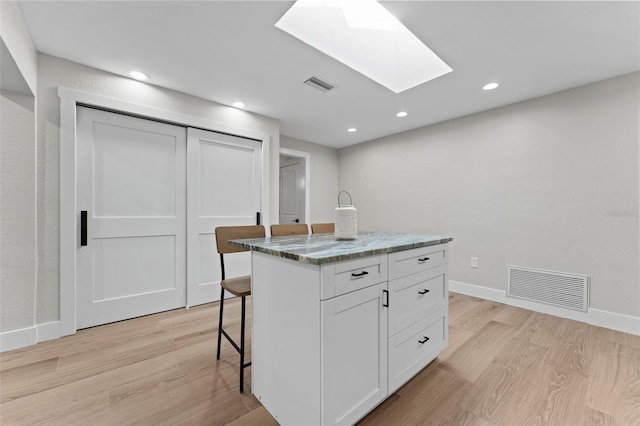 kitchen with light hardwood / wood-style flooring, a center island, white cabinetry, a skylight, and a breakfast bar area