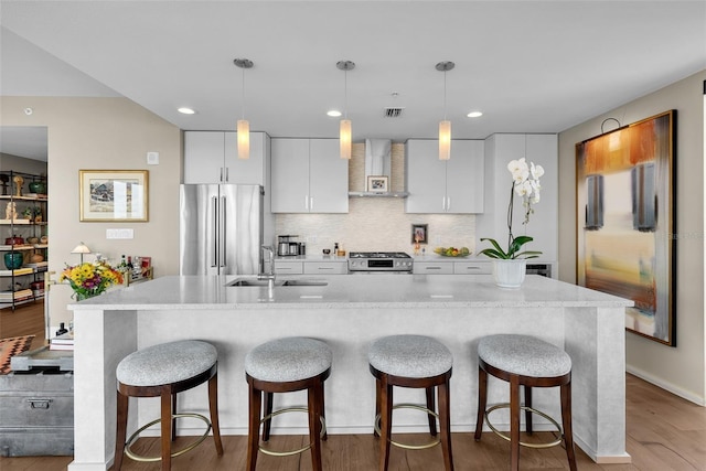 kitchen with wall chimney range hood, sink, white cabinetry, hanging light fixtures, and stainless steel appliances