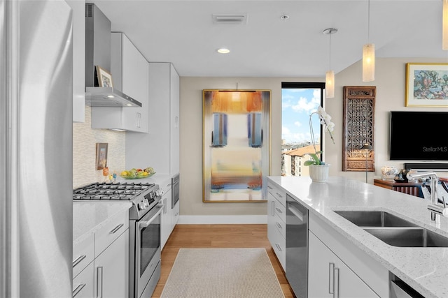 kitchen with sink, white cabinetry, hanging light fixtures, stainless steel appliances, and wall chimney exhaust hood