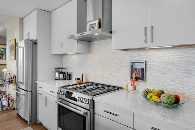 kitchen with white cabinets, backsplash, stainless steel appliances, light stone countertops, and wall chimney exhaust hood