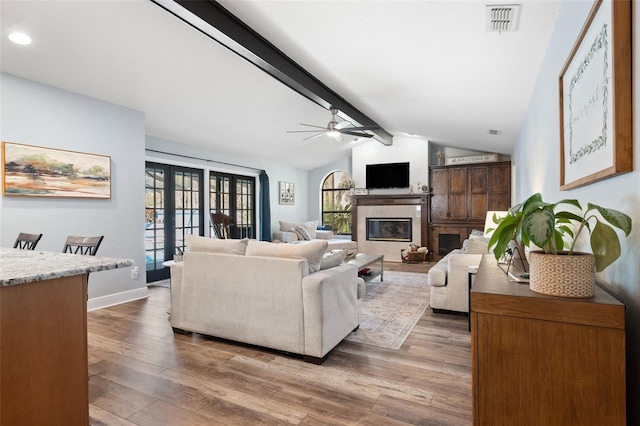 living room featuring french doors, wood-type flooring, lofted ceiling with beams, ceiling fan, and a tiled fireplace