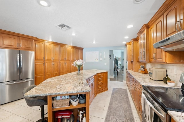 kitchen with a kitchen island, appliances with stainless steel finishes, tasteful backsplash, a kitchen bar, and light stone counters