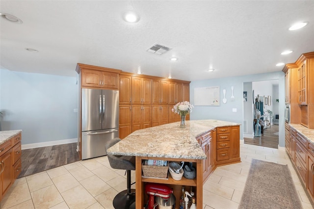 kitchen with light tile patterned floors, stainless steel refrigerator, a center island, light stone counters, and a kitchen bar