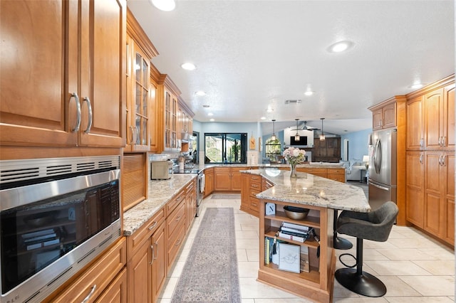 kitchen featuring pendant lighting, a kitchen breakfast bar, a center island, light stone counters, and stainless steel appliances