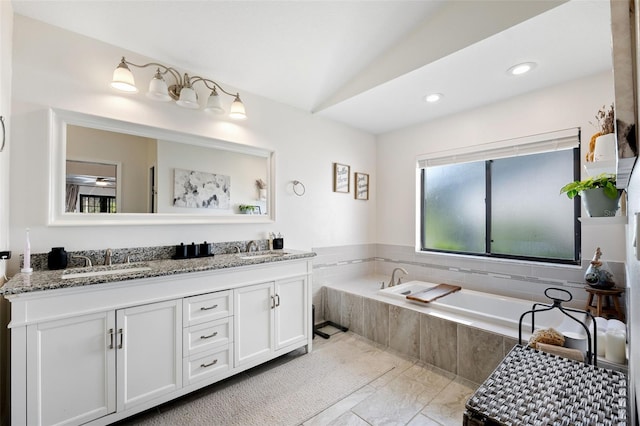 bathroom featuring vanity, a relaxing tiled tub, and vaulted ceiling