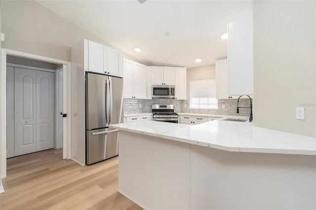 kitchen with stainless steel appliances, light stone countertops, white cabinets, sink, and kitchen peninsula