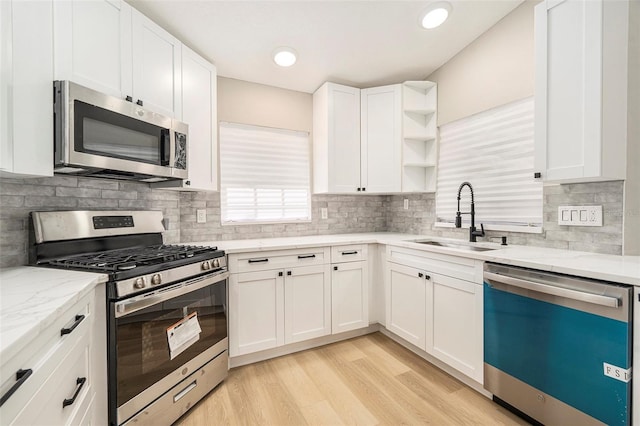 kitchen with light stone countertops, light hardwood / wood-style floors, sink, appliances with stainless steel finishes, and white cabinets