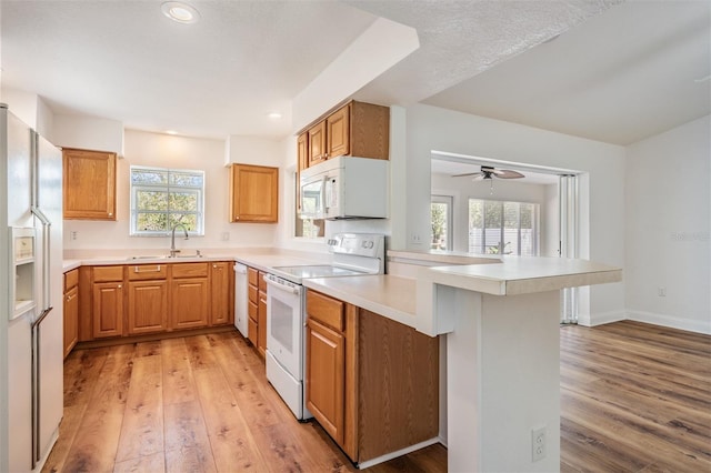 kitchen featuring a peninsula, white appliances, light wood-type flooring, and a sink