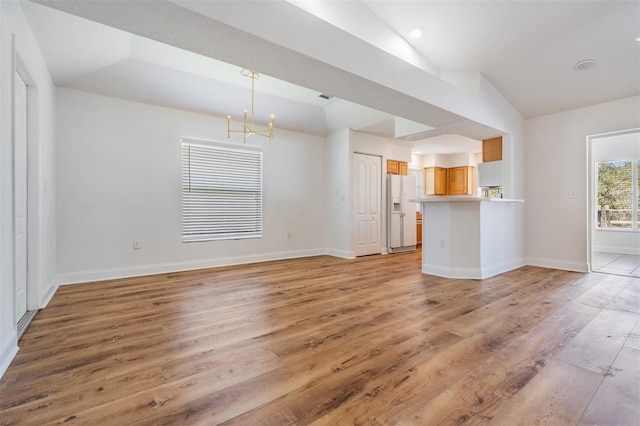 unfurnished living room featuring light wood-style floors, a notable chandelier, vaulted ceiling, and baseboards