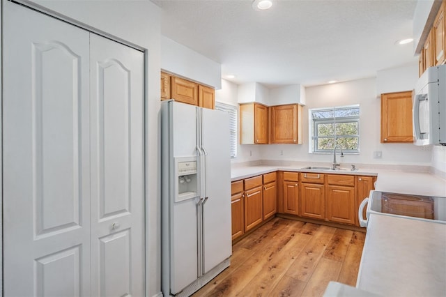 kitchen featuring white appliances, light wood-style flooring, light countertops, a sink, and recessed lighting