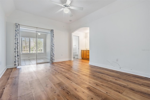 empty room featuring a ceiling fan, arched walkways, baseboards, and light wood finished floors