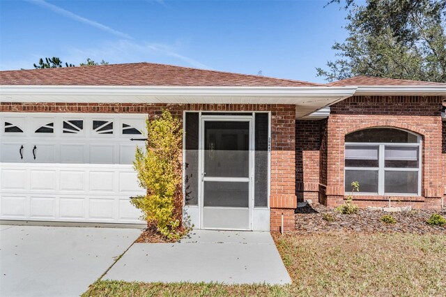 doorway to property with a garage, roof with shingles, and brick siding