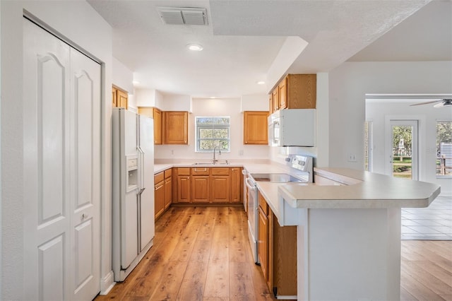 kitchen featuring a peninsula, white appliances, a sink, visible vents, and light wood finished floors