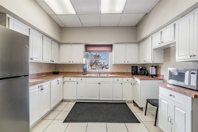 kitchen with a paneled ceiling, light tile patterned floors, stainless steel appliances, and a sink