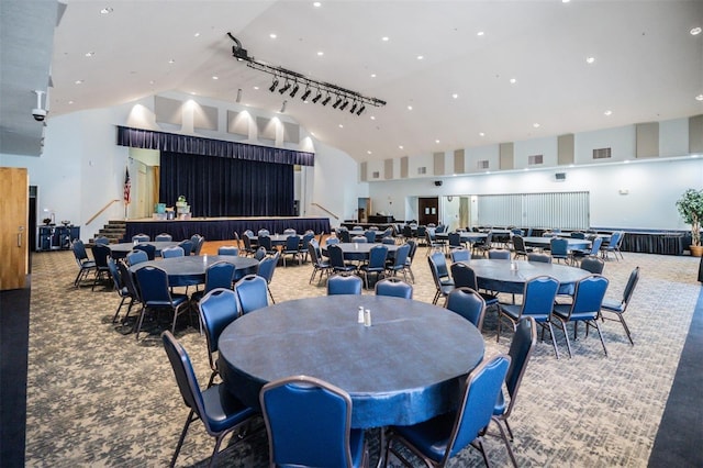 dining space featuring carpet floors, rail lighting, visible vents, high vaulted ceiling, and stairs