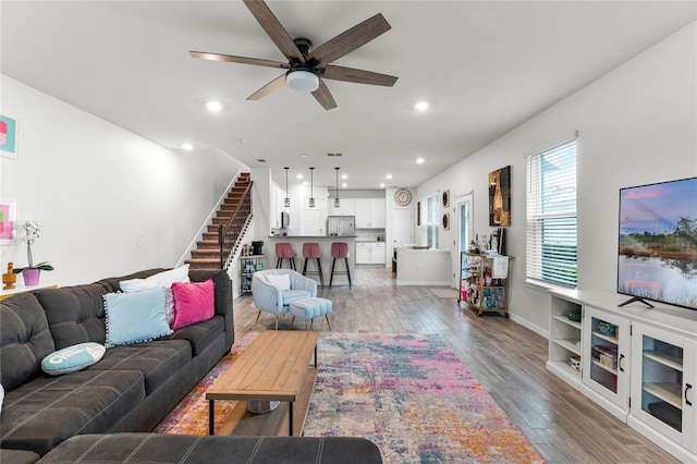 living area with ceiling fan, recessed lighting, wood finished floors, baseboards, and stairs