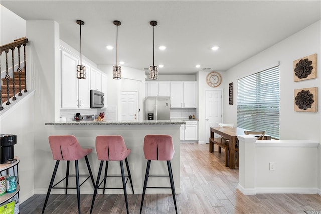 kitchen featuring light wood finished floors, appliances with stainless steel finishes, light stone counters, white cabinetry, and pendant lighting