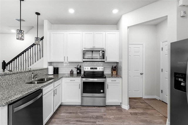 kitchen with stone counters, pendant lighting, stainless steel appliances, white cabinets, and a sink