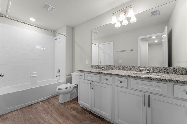 bathroom featuring double vanity, visible vents, toilet, wood finished floors, and tub / shower combination