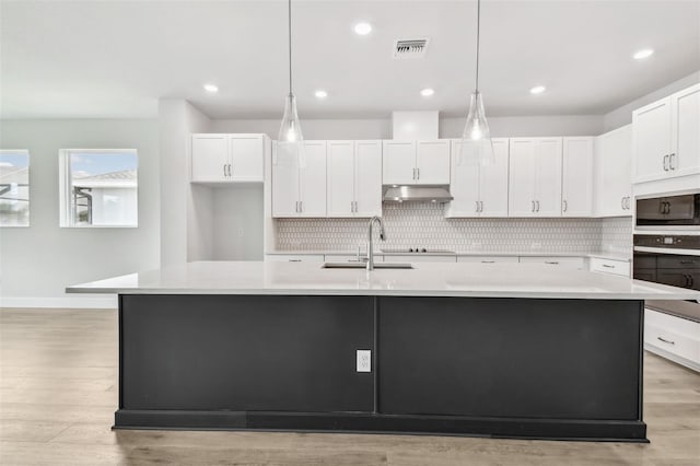 11885 Richmond Trl, Parrish, FL 34219 - kitchen with under cabinet range hood, tasteful backsplash, white cabinetry, light countertops, and stainless steel oven