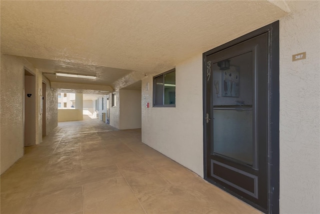 corridor featuring a textured ceiling and a textured wall